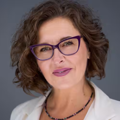 Fotograf headshot Leszno – biznesowy portret Beaty Sobolewskiej-Lipnickiej, kobiety o krótkich kręconych włosach i okularach, w jasnej marynarce, na neutralnym tle.