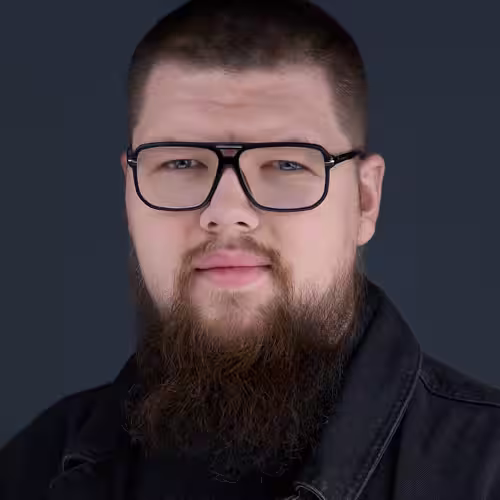 Fotograf headshot Leszno – biznesowy portret Jakuba Lipnickiego, mężczyzny z krótkimi włosami, brodą i okularami, w ciemnym stroju, na neutralnym tle.