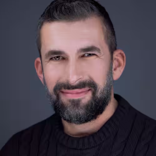 Fotograf headshot Leszno – biznesowy portret Macieja Sobolewskiego, mężczyzny z krótkimi włosami i brodą, w ciemnym swetrze, na neutralnym tle.