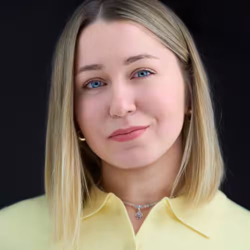 Fotograf headshot Leszno – biznesowy portret Oksany Kiziny, kobiety o jasnych włosach i niebieskich oczach, w żółtej bluzce, na ciemnym tle.
