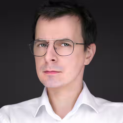 Fotograf headshot Leszno – biznesowy portret Szymona Poczwardowskiego, mężczyzny w okularach i białej koszuli, na ciemnym tle.