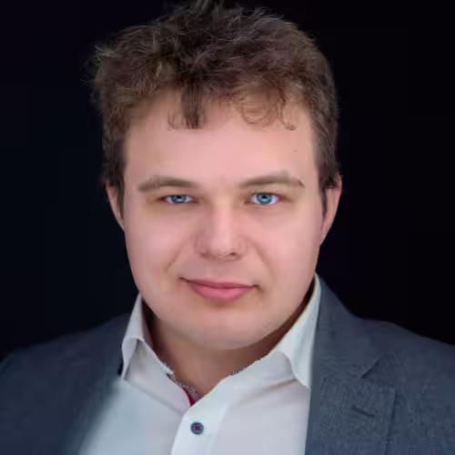 Fotograf headshot Leszno – biznesowy portret Szymona Golemięca, mężczyzny o jasnej cerze i niebieskich oczach, w białej koszuli i szarej marynarce, na ciemnym tle.