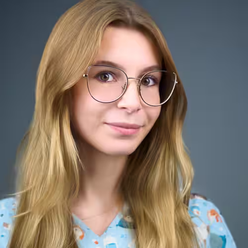 Fotograf headshot Leszno – biznesowy portret Zuzi Wojciechowskiej-Rękoś, kobiety o długich jasnych włosach w okularach, w kolorowej bluzce, na neutralnym tle.